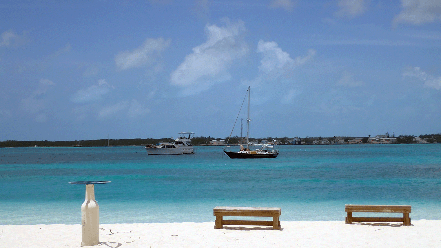 Beach scene with boats in the water and a clear blue sky.