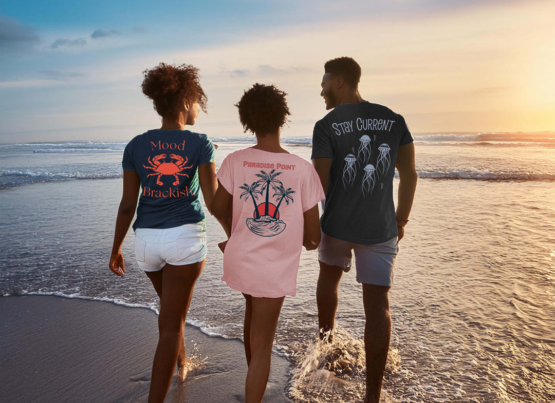Three people on a beach wearing t-shirts with designs and text.