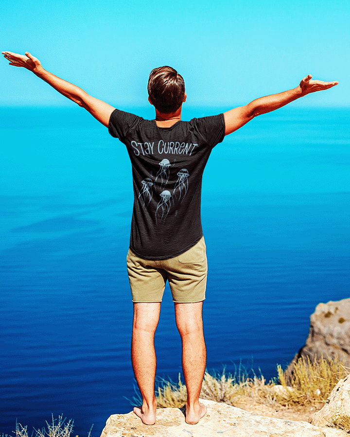 Person standing on a cliff overlooking a blue sea with arms outstretched