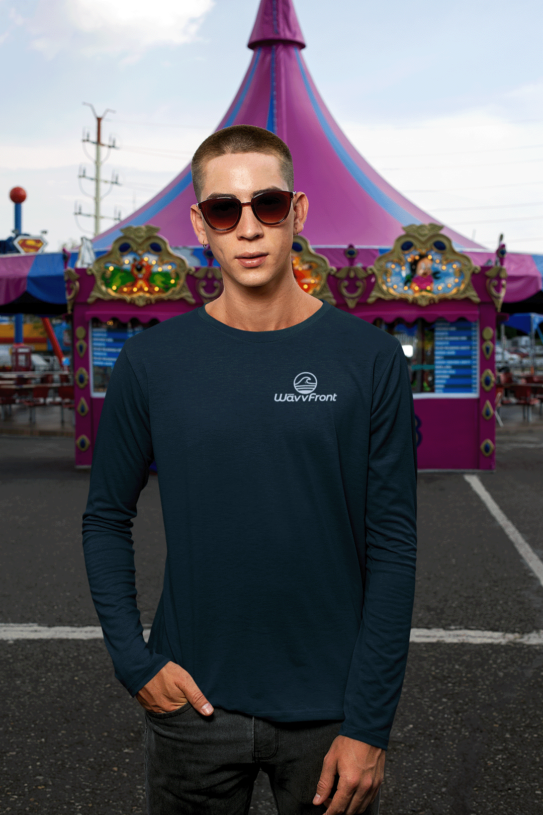 Man wearing sunglasses and a navy long-sleeve shirt with a logo in front of a colorful circus tent.