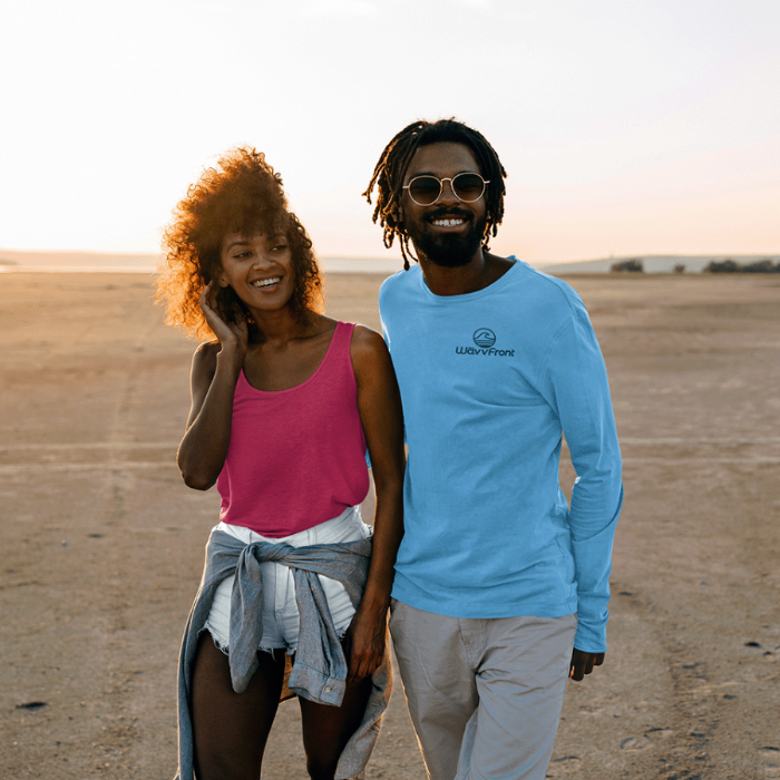 Two people standing together in a desert landscape, one wearing a pink top and denim jacket, the other in a blue long-sleeve shirt with a logo.